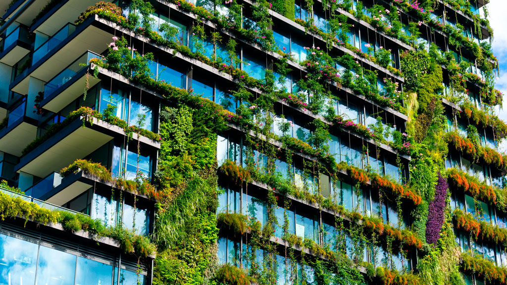 A glass building with plants and flowers growing down the sides of it